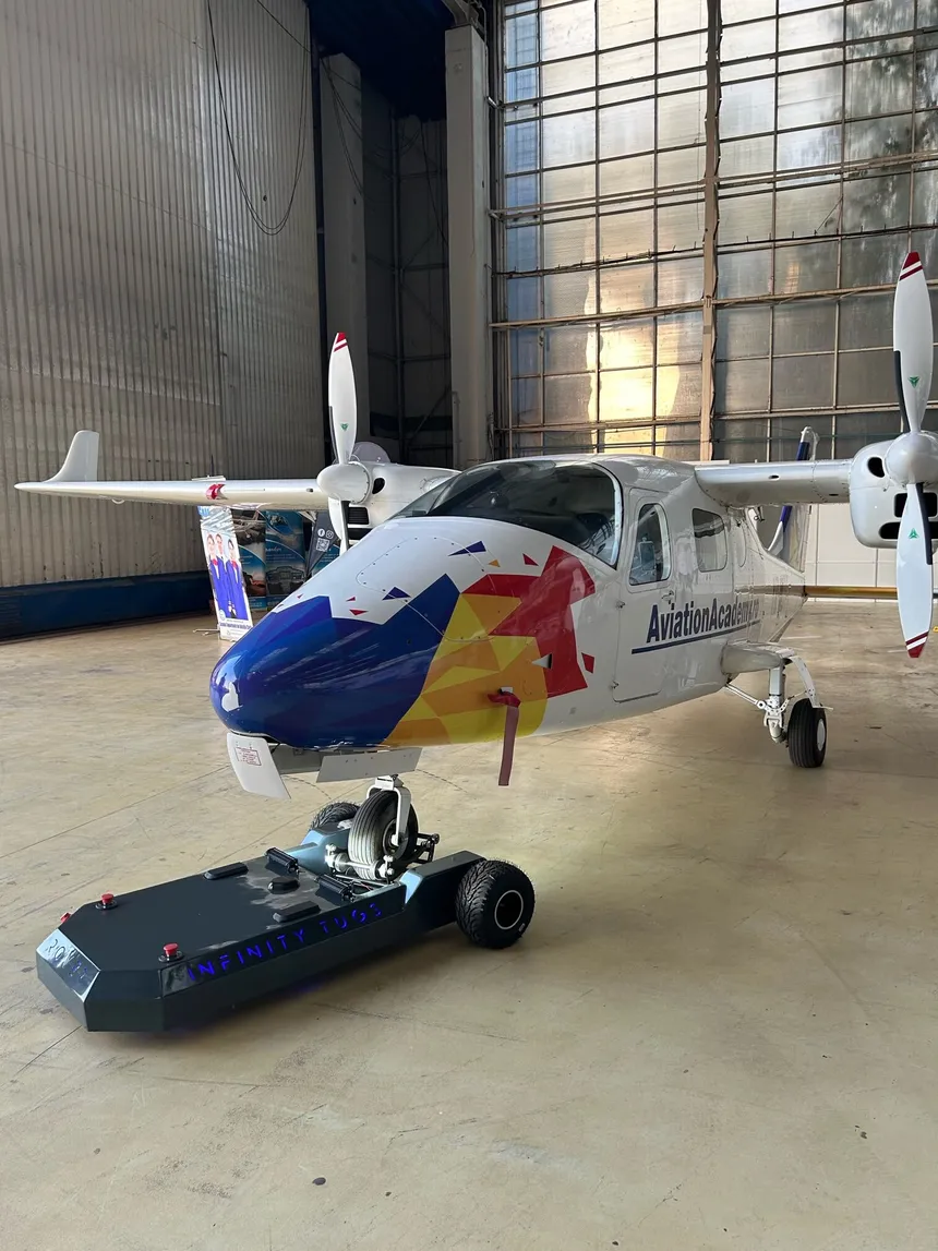 Dark graphite ROVER remote controlled aircraft tug under the nose wheel of a twin-engine trainer in a hangar